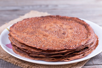 Stack of thin chocolate pancakes, crepes on white plate on the table