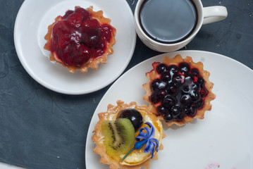 Assorted Fruit Tarttlets, or Basket, Cakes with Cream and Berries on White Plate with cup of coffee over Gray Background for holiday. Flat Lay. copy space for Text.
