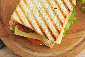 Sandwich of fried bread on a wooden tray. As the filling for the sandwich used chicken breast, bacon, green salad, cheese, tomatoes and pickles. View from above. Close-up. Macro photography.