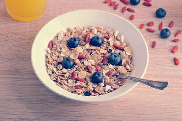 Muesli in a white plate of oatmeal and corn flakes, with airy rice, goji berries and blueberries. Beige wood background.