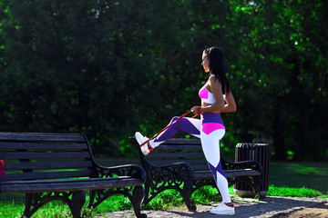 Sporty woman with dark hair does exercises with the expander on a Park bench.