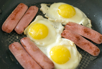 Fried eggs with sausages, 3 fried eggs, several sausages on a black frying pan