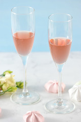 Two glasses with pink wine. In the frame flowers and meringue in light pink colors. Light background. Close-up. Vertical orientation of the frame.