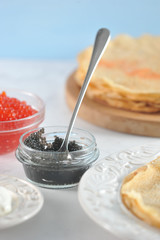 Pancakes thin on a round wooden tray and on a plate. There are two cups with red and black caviar. There is sour cream on the saucer. Light background. Vertical orientation of the frame.