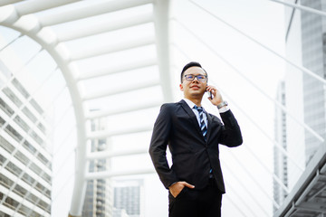 Professional Asian business man walking along sidewalk and talking on mobile phone in urban city. Business and technology concepts