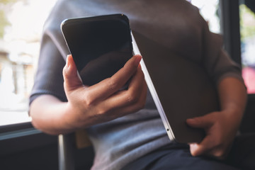 Closeup image of a woman using and looking at smart phone while holding laptop