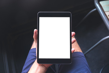 Mockup image of a man's hand holding black tablet pc with blank white screen on thigh