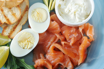 Red salted fish, toast, hard boiled egg, soft cream cheese, slices of lime on a blue plate. Light background. View from above. Close-up. Macro photography.