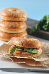 Beagle with a filling of salted salmon, arugula, cucumber, soft cheese. Beigle on kraft paper. In the background there is one more Beigle. Light background. Close-up. Macro photography.