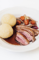 Plate with roasted duck breast, roasted vegetables such as carrots, red onions and scallions with traditional Franconian or Bavarian potato dumplings and gravy as typical German sunday roast dish