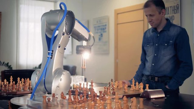 Robot hand manipulator moves the chess figure. Futuristic concept. Playing chess with a man.