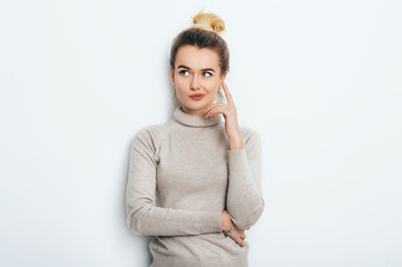 Portrait of attractive thoughtful young female wearing her blonde hair in knot holding forefinger...