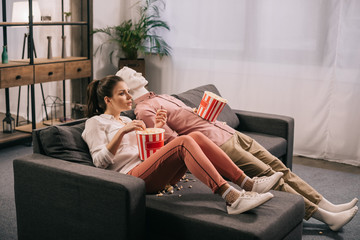 woman eating popcorn while watching film together with manikin at home, perfect relationship dream concept