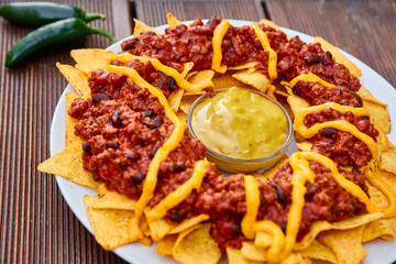 National Mexican and Chilean dish on a wooden table. Homemade potato chips with tomato sauce, beans and minced meat. Mustard sauce in the middle of the dish. Decorated with green peppers and tomatoes.