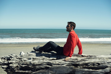 Retrato de hombre joven vestido de rojo frente a paisaje de playa minimalista con un amplio cielo...