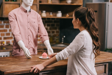 selective focus of woman giving cupcake to manikin in casual clothing, loneliness concept