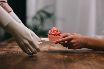 cropped shot of woman and mannequin holding plate with cupcake, unrequited love concept