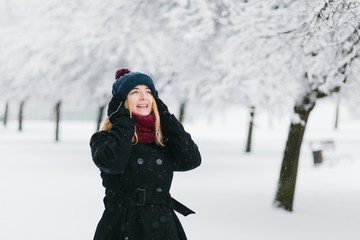 Fototapeta na wymiar Young caucasian blonde girl in black coat and red knitted scarf walks in winter park