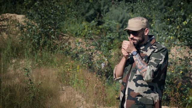 Brutal bearded soldier in sunglasses Smoking cigarette in forest background