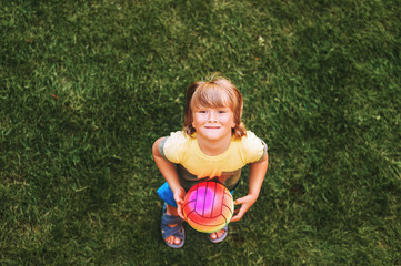 Little boy playing with the ball outside on green lawn, top view
