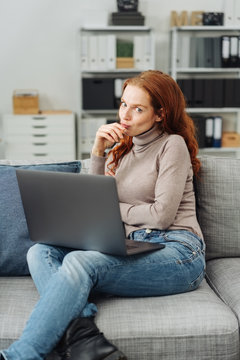 Young woman sitting with laptop on sofa at home