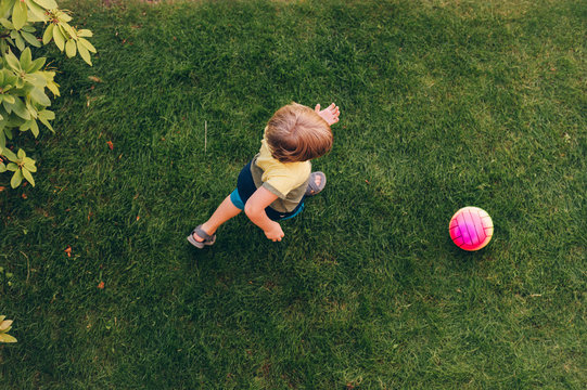 Little boy playing with the ball outside on green lawn, top view