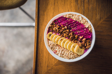 Superfood tropical smoothie bowl with dragon fruits, banana, granola on a wooden coffee table. Minimal food photography concept. Flatlay, copyspace