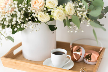 Obraz na płótnie Canvas Blush wedding bouquet with roses, baby's breath and eucaluptus in wooden tray with coffee and hedphones