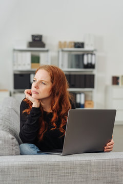 Young thoughful woman sitting with laptop on sofa