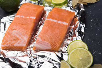 Sliced salmon fillet on a foil. Fresh raw fish with lime and spices on a baking tray. Metal black...