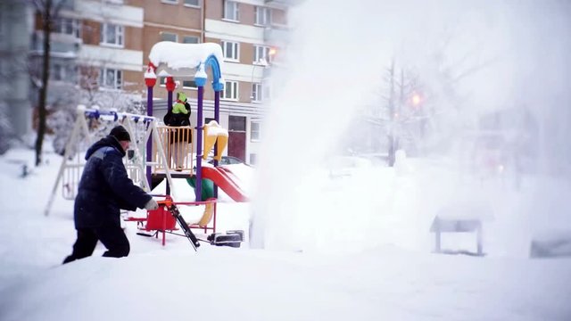 The janitor clears the track with a snowplow in the courtyard of an apartment building.
