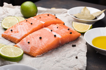 Sliced salmon fillet on a baking paper. Fresh raw fish and  lime and spices, ingredients. Metal black background