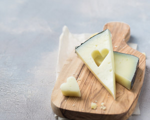 Wooden board with tasty goat cheese on concrete stone background. Cheese heart. Romantic holiday table setting. Beautiful background with blank. Restaurant concept.