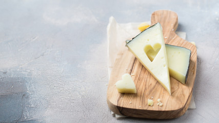 Wooden board with tasty goat cheese on concrete stone background. Cheese heart. Romantic holiday...