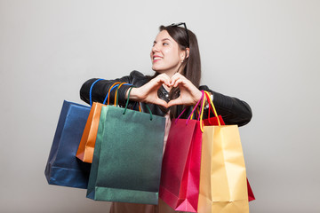 Cute teenage girl shows heart holding bags