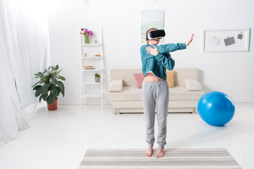 girl stretching hands with virtual reality headset on yoga mat at home