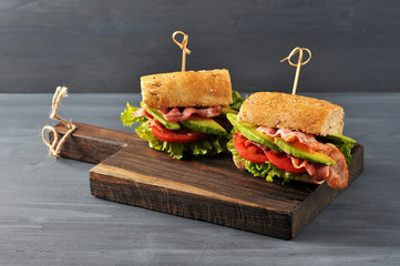 Appetizing sandwich on a wooden board. Baguette sandwich with filling from lettuce, slices of fried...