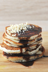 Pancakes are laid out on a wooden board. Pancakes are poured with chocolate syrup and decorated with nut crumbs. Light wooden background. Vertical orientation of the frame. Close-up.