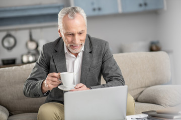 Mature businessman. Cheerful male person being at home and bowing head while staring at his laptop