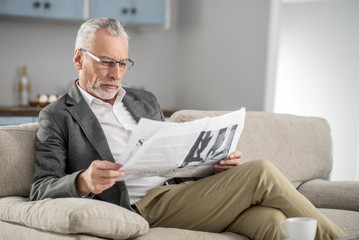 Time to relax. Concentrated bearded man pressing lips and bowing head while looking at newspaper