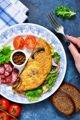 Omelette with mushrooms, cheese and spinach on a concrete blue background. Light breakfast with salami, scrambled eggs and vegetables.