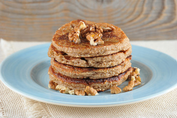 Buckwheat pancakes are lined with a slide on a blue plate. Pancakes are decorated with walnuts and honey. Under the plate is a napkin. Wooden background. Close-up.