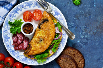 Omelette with mushrooms, cheese and spinach on a concrete blue background. Light breakfast with salami, scrambled eggs and vegetables.
