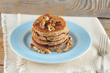 Buckwheat pancakes are lined with a slide on a blue plate. Pancakes are decorated with walnuts and honey. Under the plate is a napkin. Wooden background. Close-up.