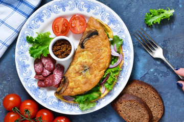 Omelette with mushrooms, cheese and spinach on a concrete blue background. Light breakfast with salami, scrambled eggs and vegetables.
