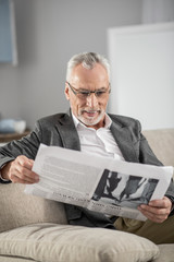Being at home. Attractive mature man holding newspaper and smiling while being at home