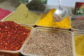The seller of spices picks up coriander in his spoon and demonstrates it