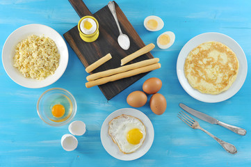 Before us, scrambled eggs, omelette, fried eggs soft-boiled eggs, two halves of a hard-boiled egg, a cup with a raw egg. In the frame of the shell. Blue background. View from above.