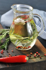 On the board is a jug with olive oil. In the oil float peppercorns, rosemary and garlic. Next a branch of rosemary, hot red pepper. In the background a napkin. Vertical orientation of the frame.