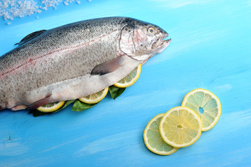 Atlantic large salmon. Salmon wasted. The abdomen of the fish is stuffed with lemon and basil. Next to salmon slices of lemons and salt. Blue wood background. View from above. Close-up.